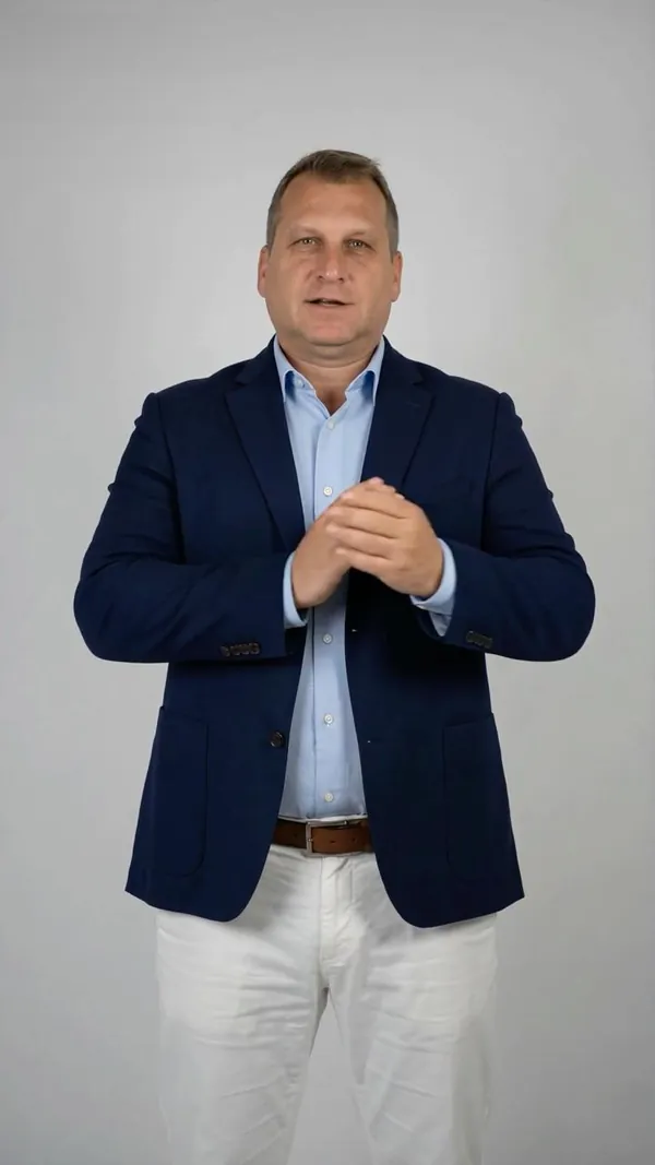 Presenter with hands clasped, speaking to the camera.