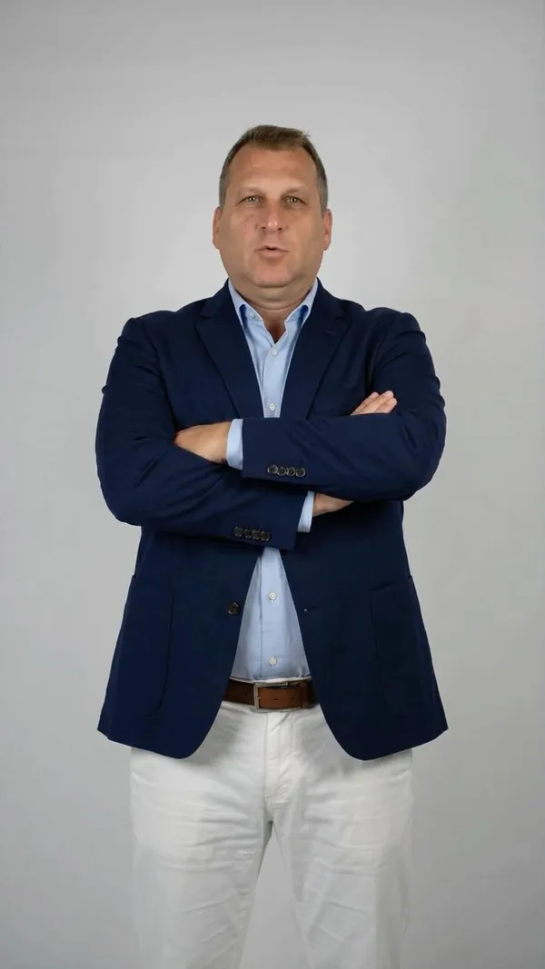 Presenter in a navy blazer standing with arms crossed, looking at the camera.