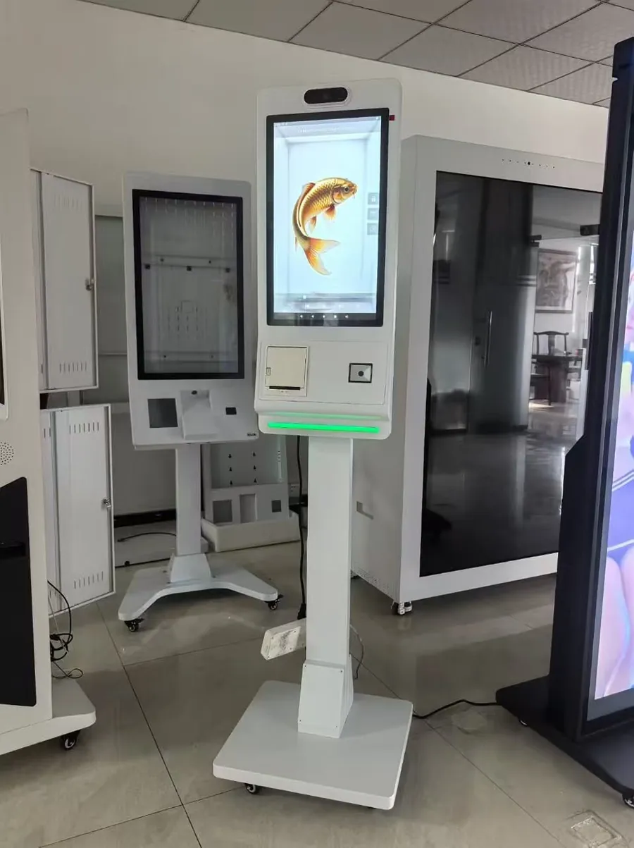 A white floor-standing kiosk with a vertical screen showing a 3D golden fish, a receipt printer, a scanner and a green status light.